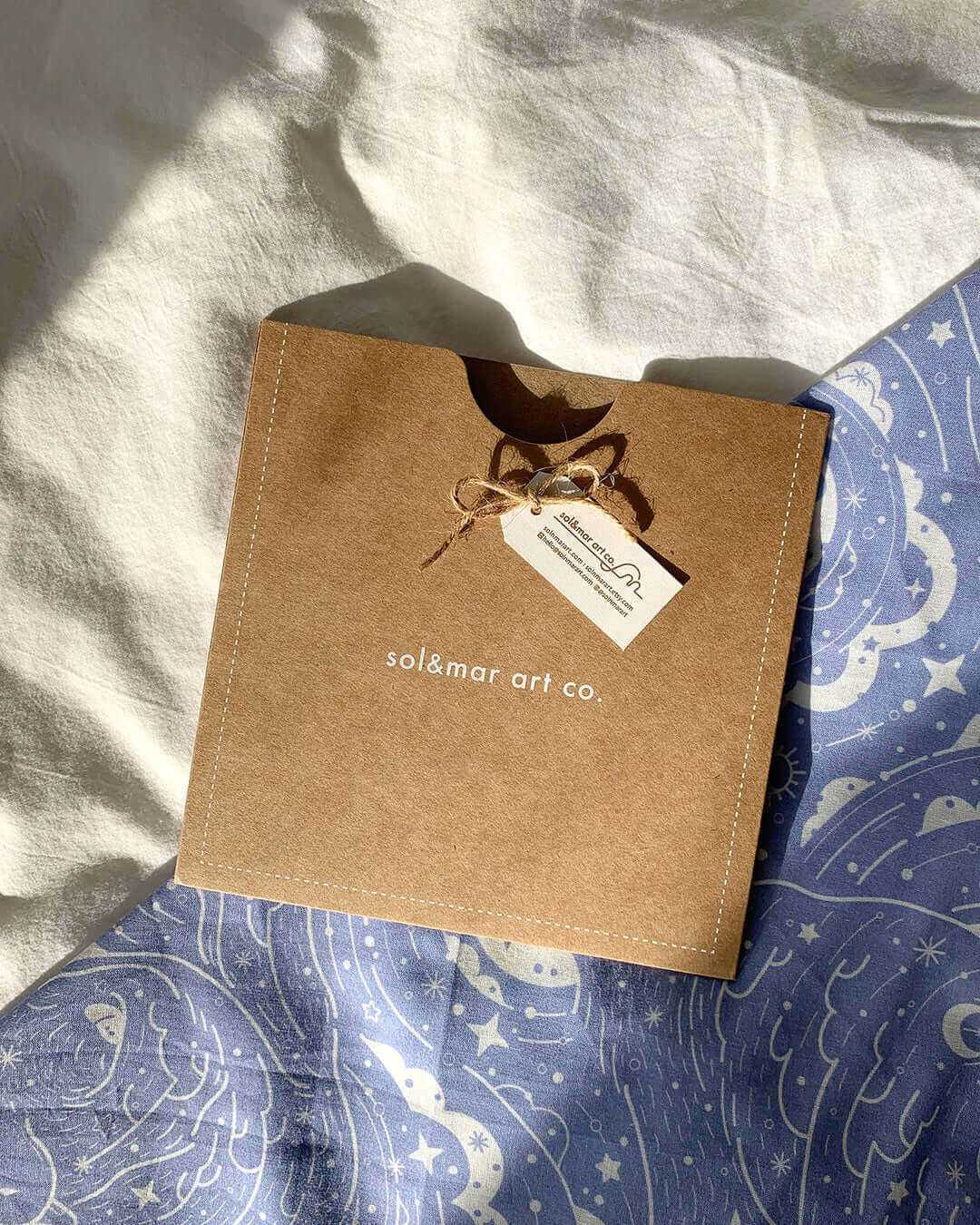Eco-friendly packaging from sol&mar art co. featuring a tag, resting on a blue patterned fabric.