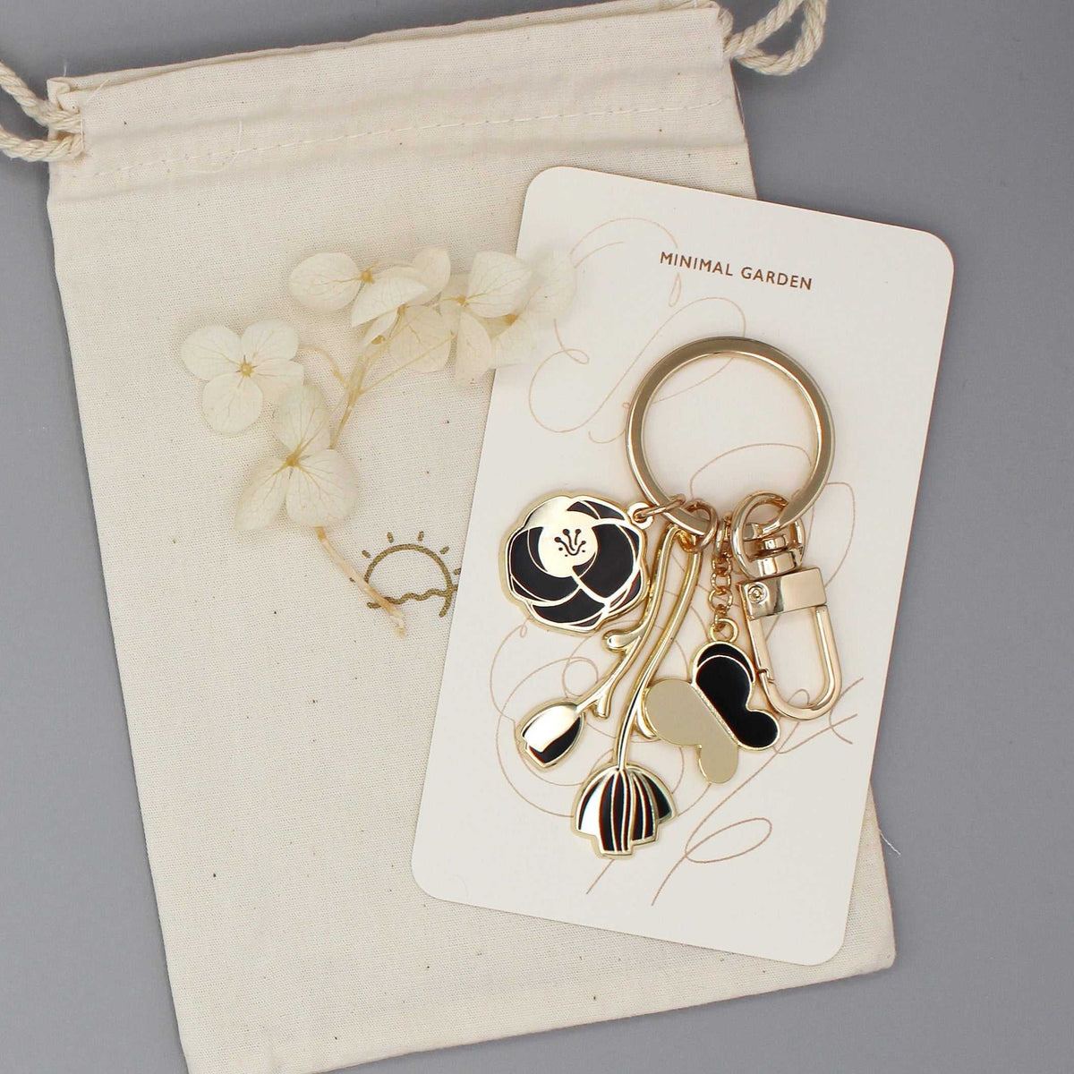 Minimal Garden keychain with black flower and butterfly charms, gold-plated metal, displayed on a card.
