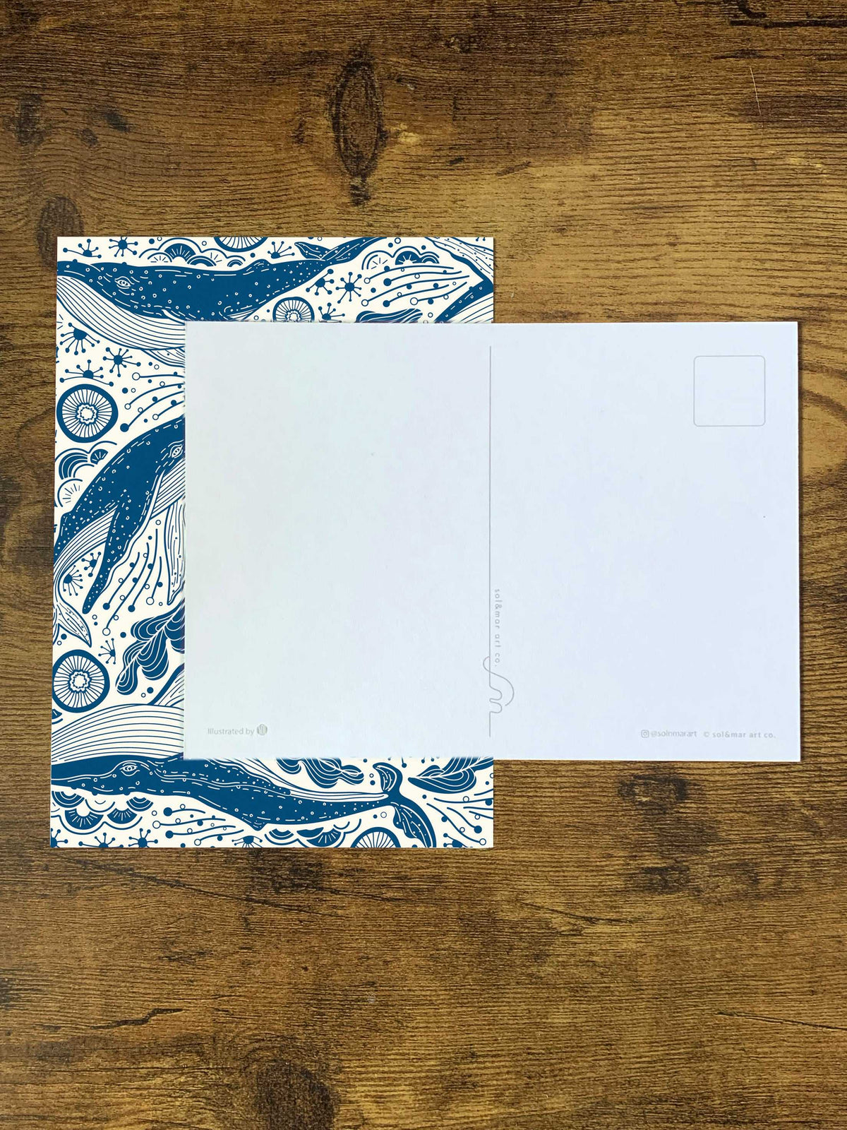 Humpback whale and ocean art postcard on a wooden surface, featuring intricate blue line designs.