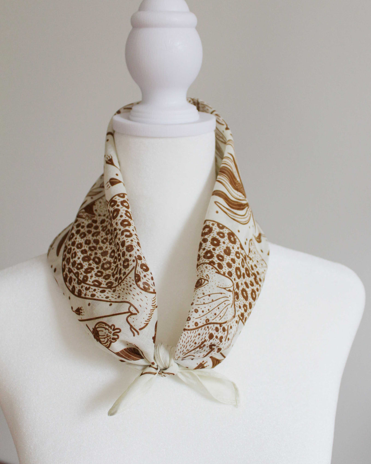 Leopard and the Sun off-white bandana scarf tied around a mannequin's neck showcasing artistic leopard design.