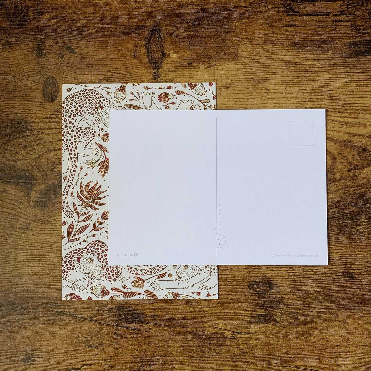 Leopard and floral patterned postcard on wooden table, featuring a blank side for writing.