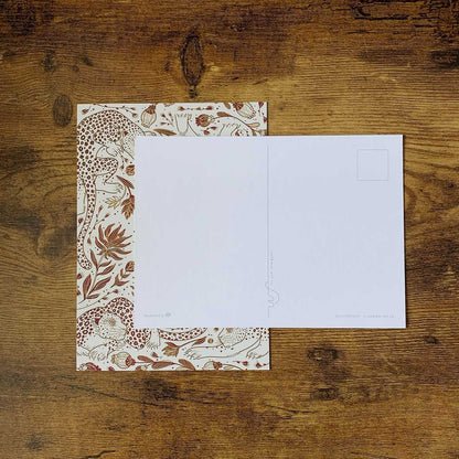 Leopard and floral patterned postcard on wooden table, featuring a blank side for writing.