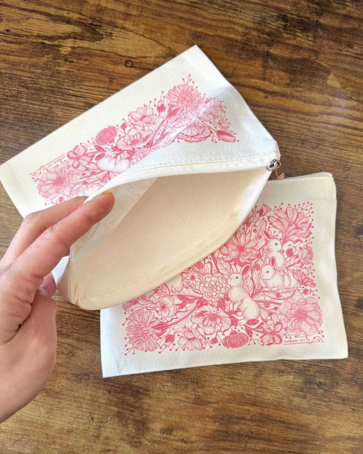 Hand holding Bunny in the Floral Breeze canvas zipper pouch, featuring floral bunny art on a flat cosmetic pouch.