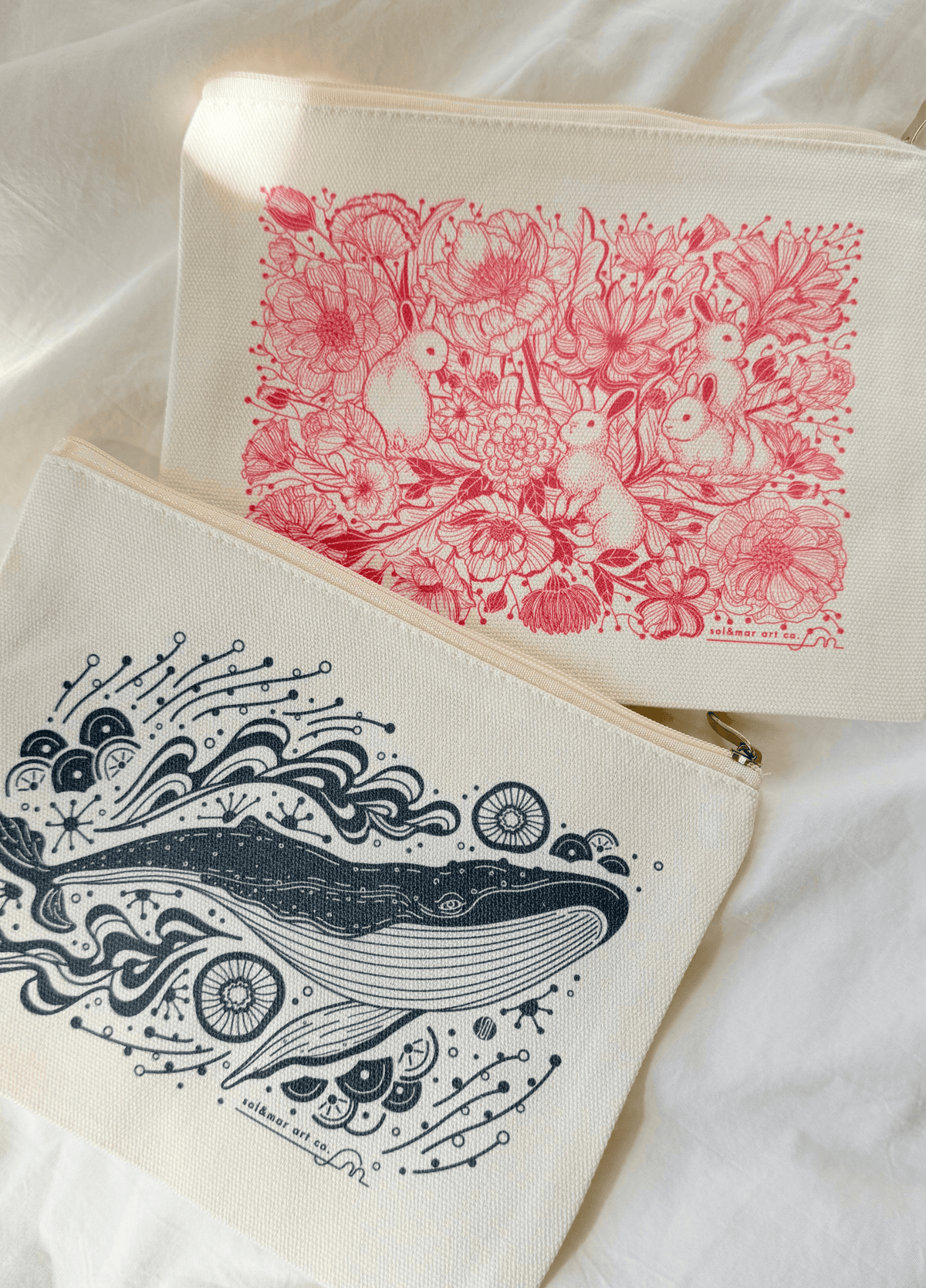 Cotton canvas zipper pouches with floral bunny and whale illustrations on a soft background.