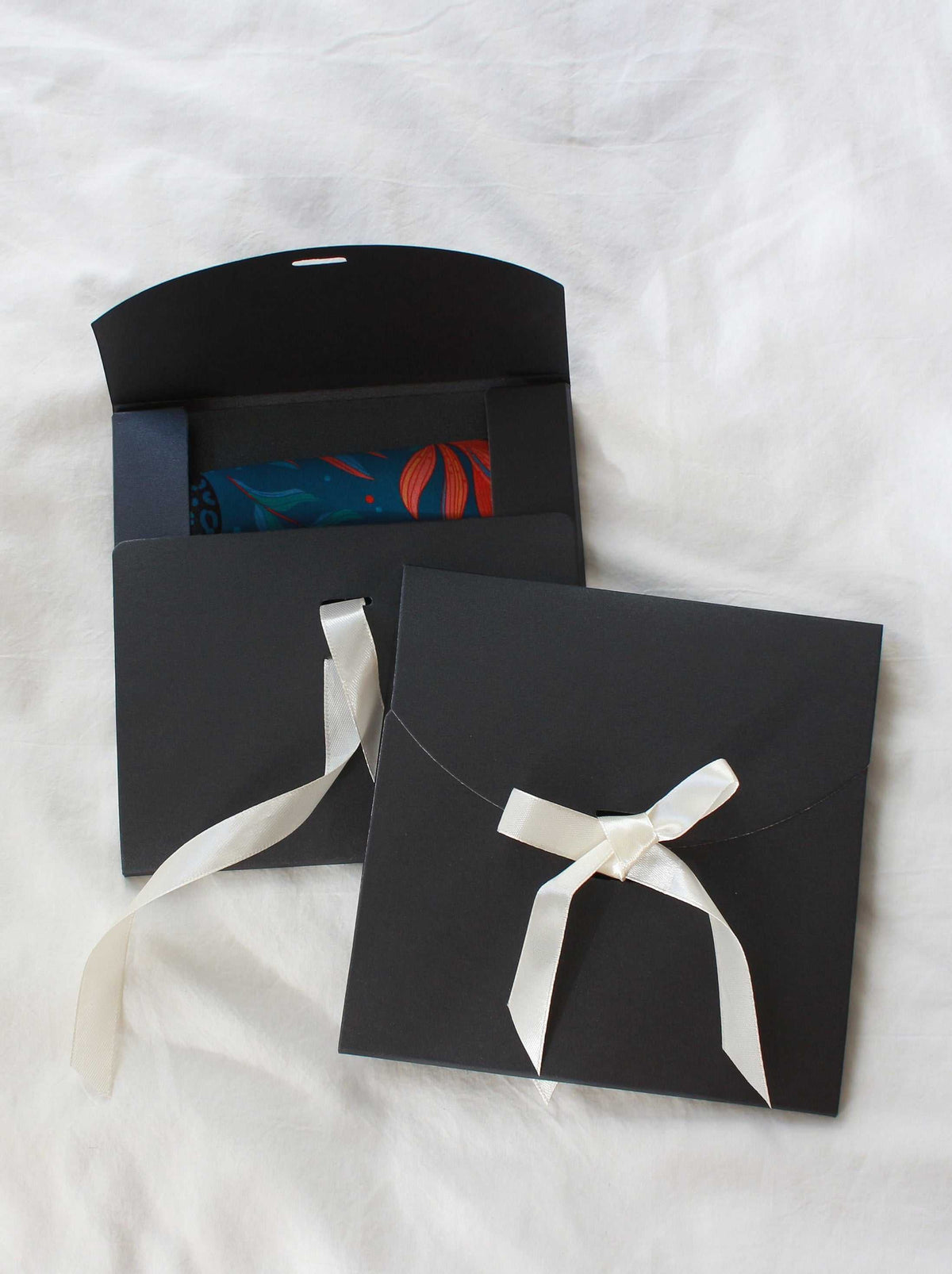 Elegant black gift envelopes with white ribbons, ideal for presenting scarves or accessories.