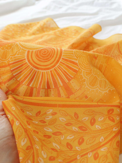 Close-up of a soft golden yellow bandana featuring intricate designs, perfect for accessorizing hair or bags.