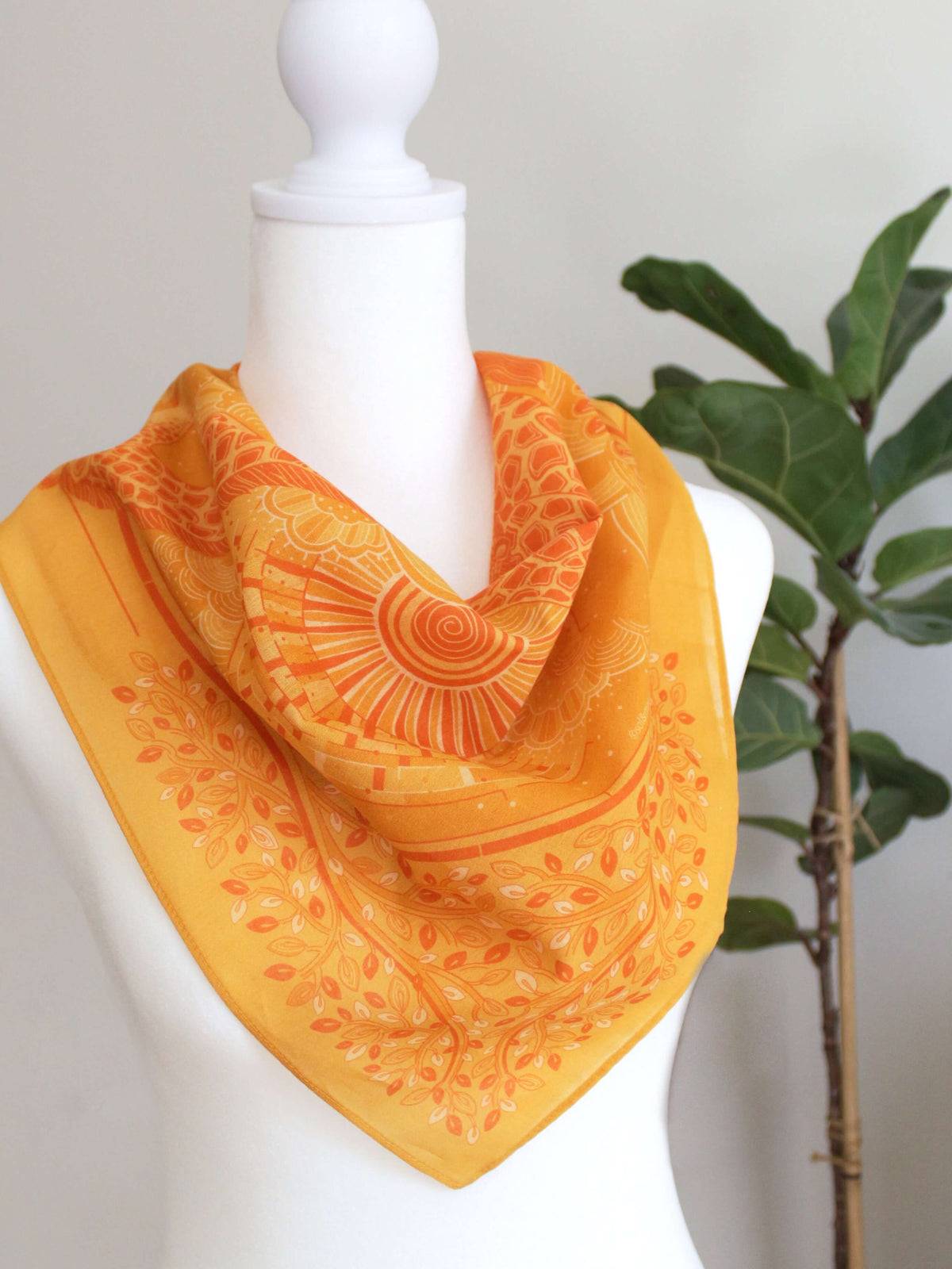 Golden yellow bandana scarf styled on a mannequin with vibrant sun and leaf patterns.