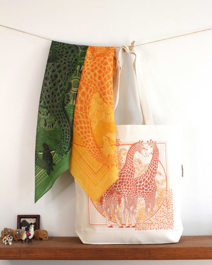 Giraffe art canvas tote bag displayed with colorful scarves on a wooden shelf.
