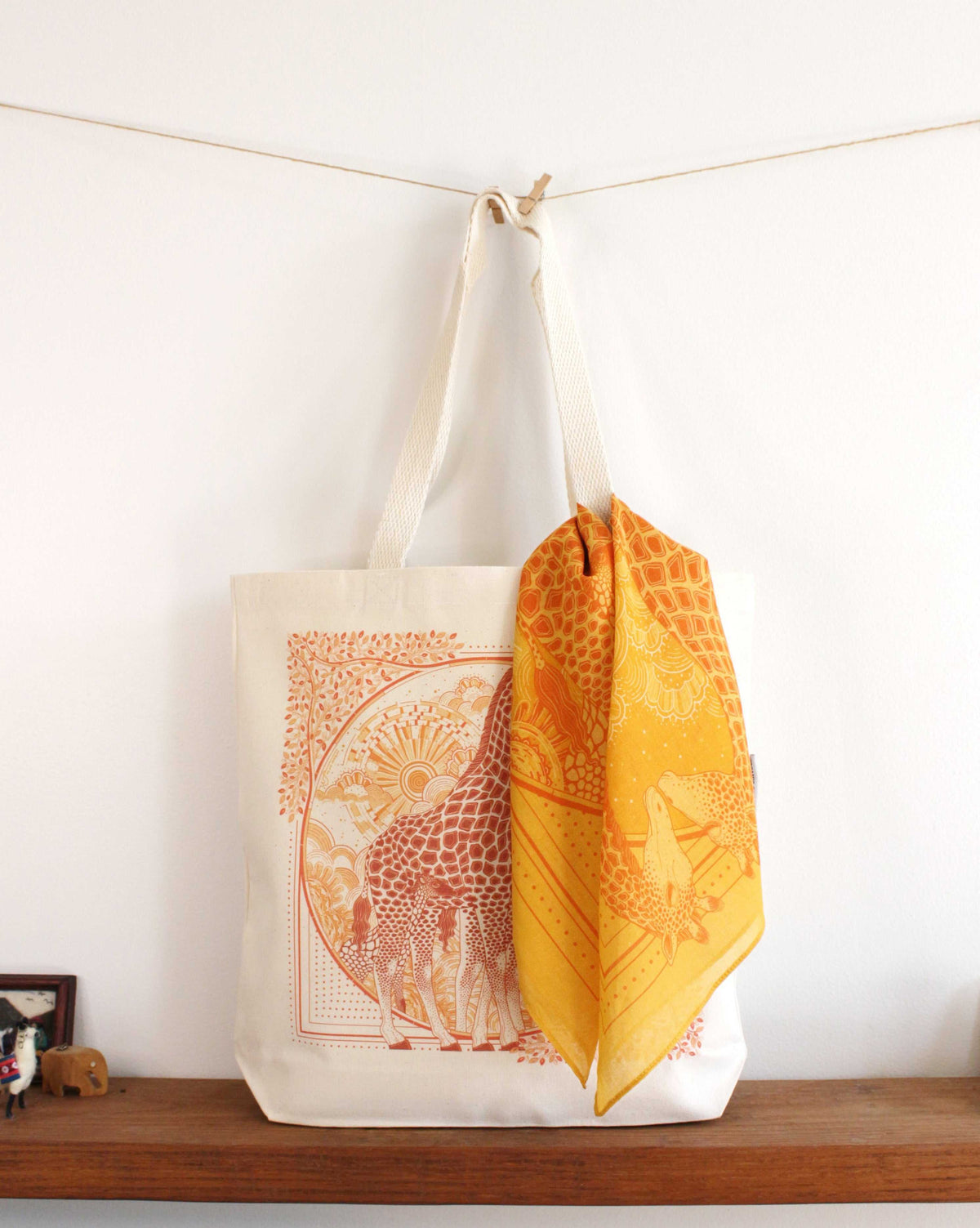 Giraffe art canvas tote bag with orange print and a matching yellow scarf displayed on a wooden shelf.