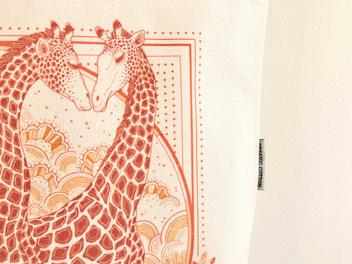 Giraffe art illustration on organic cotton canvas tote bag, featuring two giraffes in warm colors.