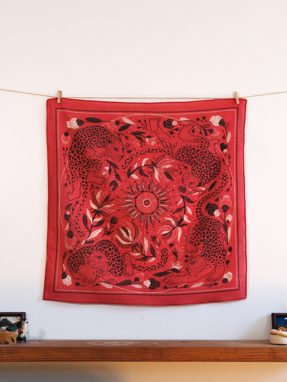 Red bandana with black and white patterns hanging on a line against a white wall.