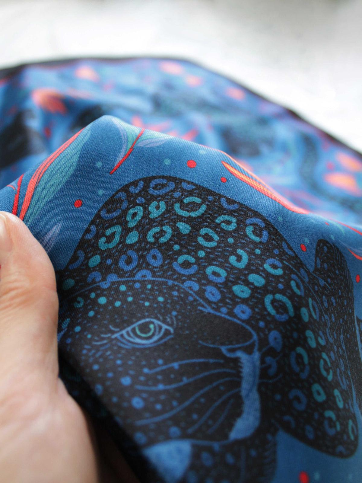 Close-up of a person's hand holding a Leopard and Tropical Flowers silk scarf, showcasing its vibrant colors and intricate design.