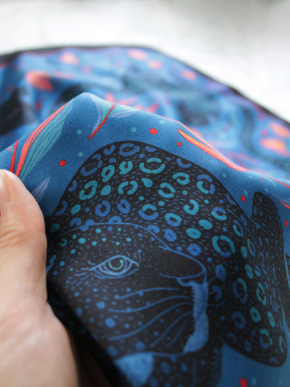 Close-up of a person's hand holding a Leopard and Tropical Flowers silk scarf, showcasing its vibrant colors and intricate design.