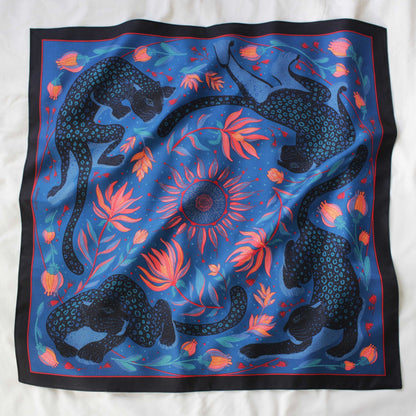 Leopard and the Sun Silk Twill Scarf featuring black leopards, sun, and tropical flowers on a blue background.