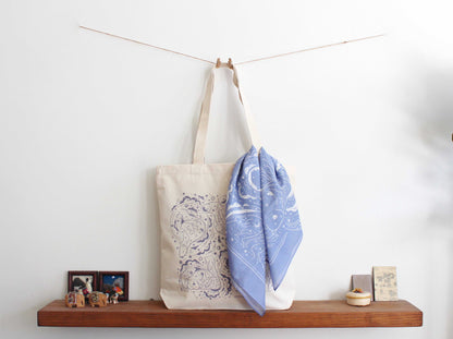 Canvas tote bag with intricate design displayed on shelf, complemented by a blue scarf.