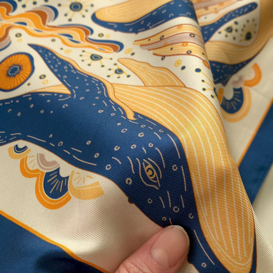 Hand holding a colorful silk twill scarf featuring an illustrated Humpback Whale design.