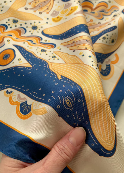 Hand holding a colorful silk twill scarf featuring an illustrated Humpback Whale design.