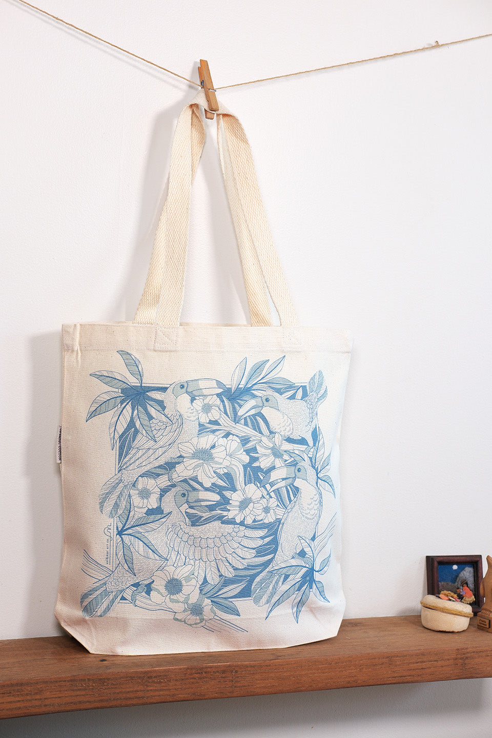 Tote bag with blue floral design hanging on a line against a white wall.
