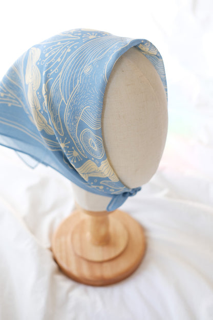 Light blue whale and ocean bandana scarf displayed on a mannequin head, showcasing intricate art design.