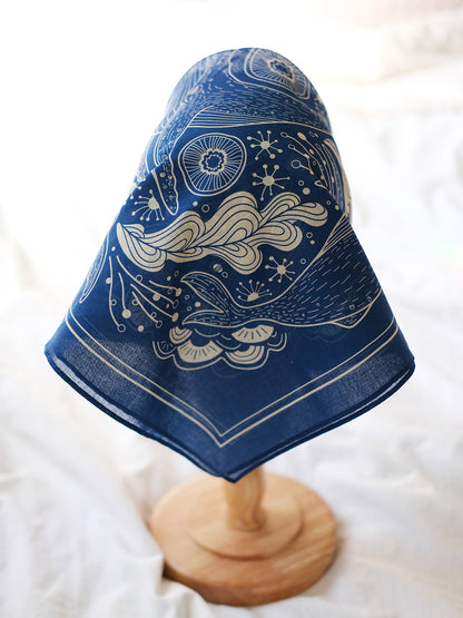 Navy whale and ocean bandana scarf displayed on a wooden stand, featuring intricate ocean-themed artwork.