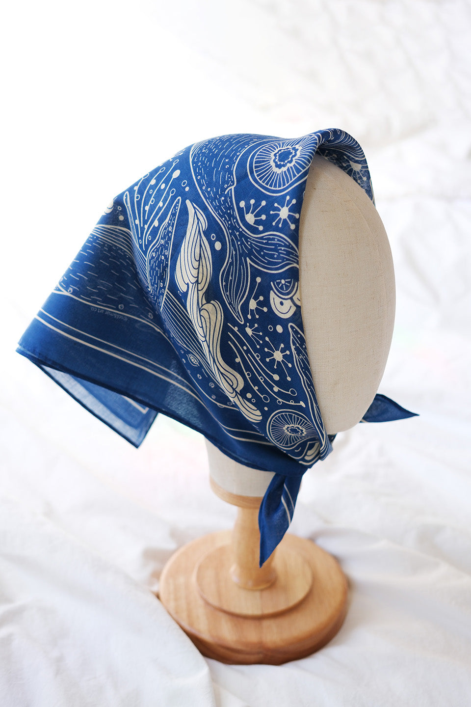 Navy whale and ocean bandana scarf displayed on a stand, featuring intricate ocean art design.
