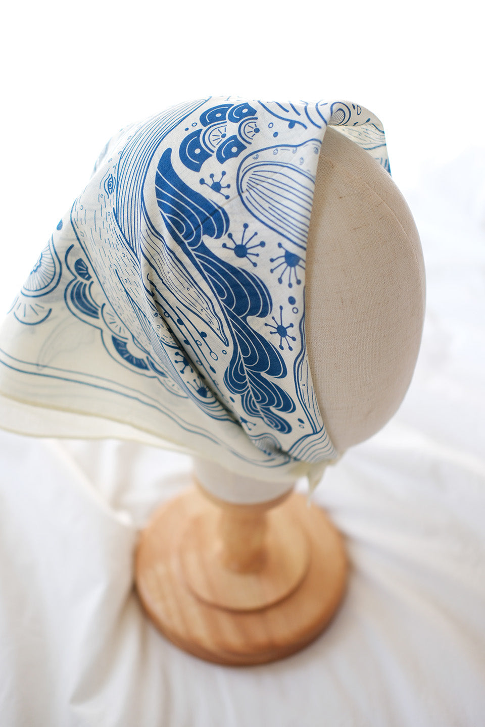 Whale and Ocean bandana scarf displayed on a mannequin head, featuring blue ocean wave designs on off-white fabric.