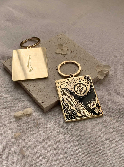 Humpback whale and ocean enamel keychain on a textured surface, showcasing intricate design details.