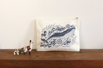 Canvas zipper pouch featuring whale art on a wooden surface with small figurines beside it.