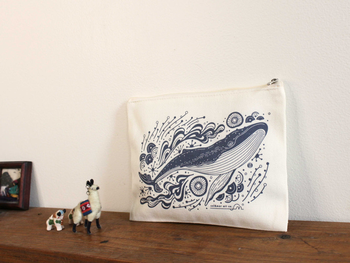Whale and ocean canvas zipper pouch on wooden shelf, featuring intricate humpback whale illustration.