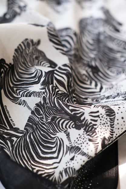 Close-up of a black and white bandana scarf featuring an artistic illustration of zebras.