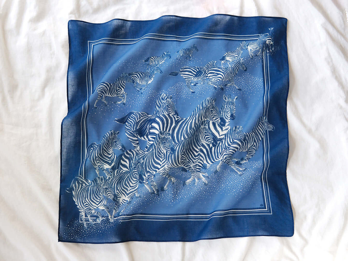 Blue zebra bandana scarf featuring a herd of zebras, 22x22 inches, soft cotton for versatile styling and year-round wear.