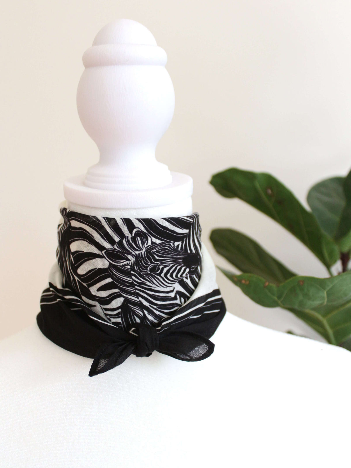 Black and white zebra-patterned bandana scarf tied around a mannequin's neck against a green background.