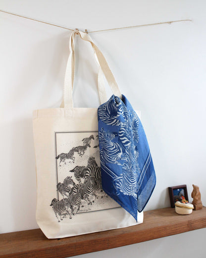 Zebra art canvas tote bag with blue patterned scarf, displayed on a wooden shelf.