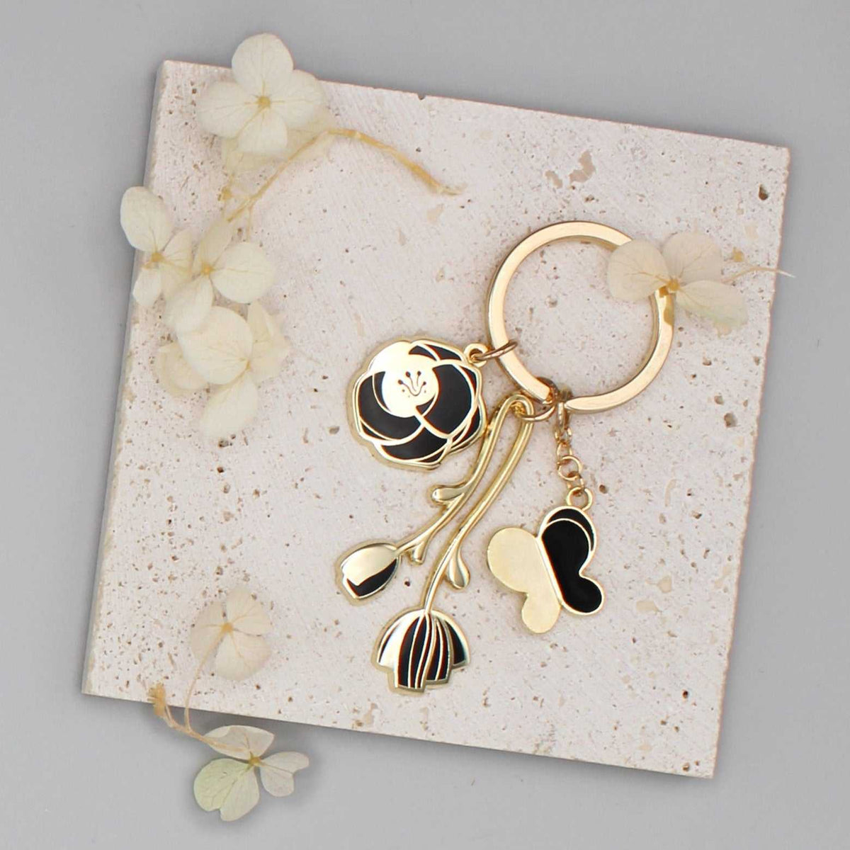 Minimal Garden Keychain featuring black rose, peony, and butterfly charms, set on a textured display card.