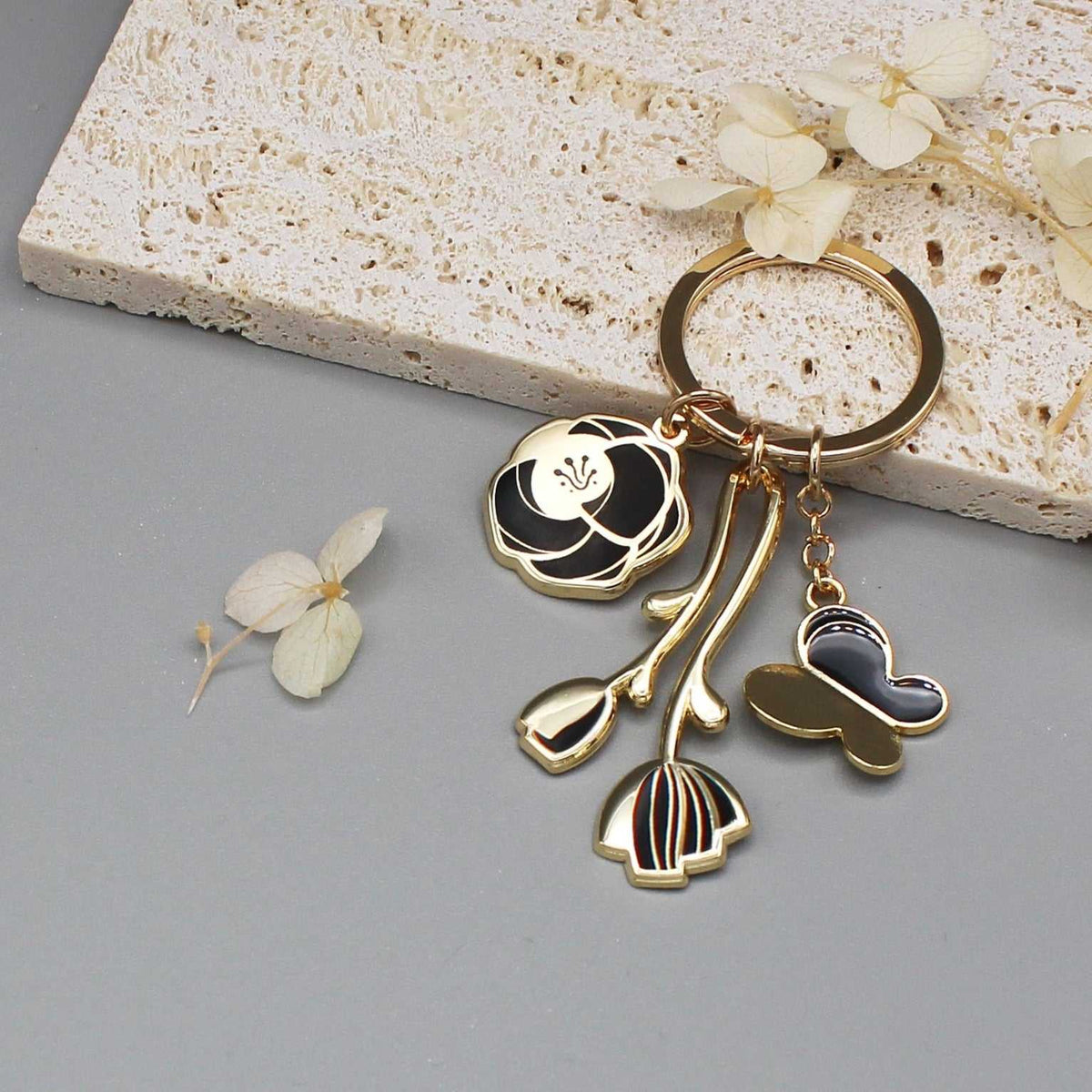 Minimal Garden Keychain in black with gold-plated flower and butterfly charms, displayed on a neutral background.