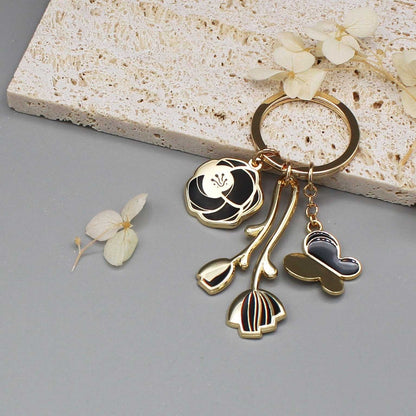 Minimal Garden Keychain in black with gold-plated flower and butterfly charms, displayed on a neutral background.