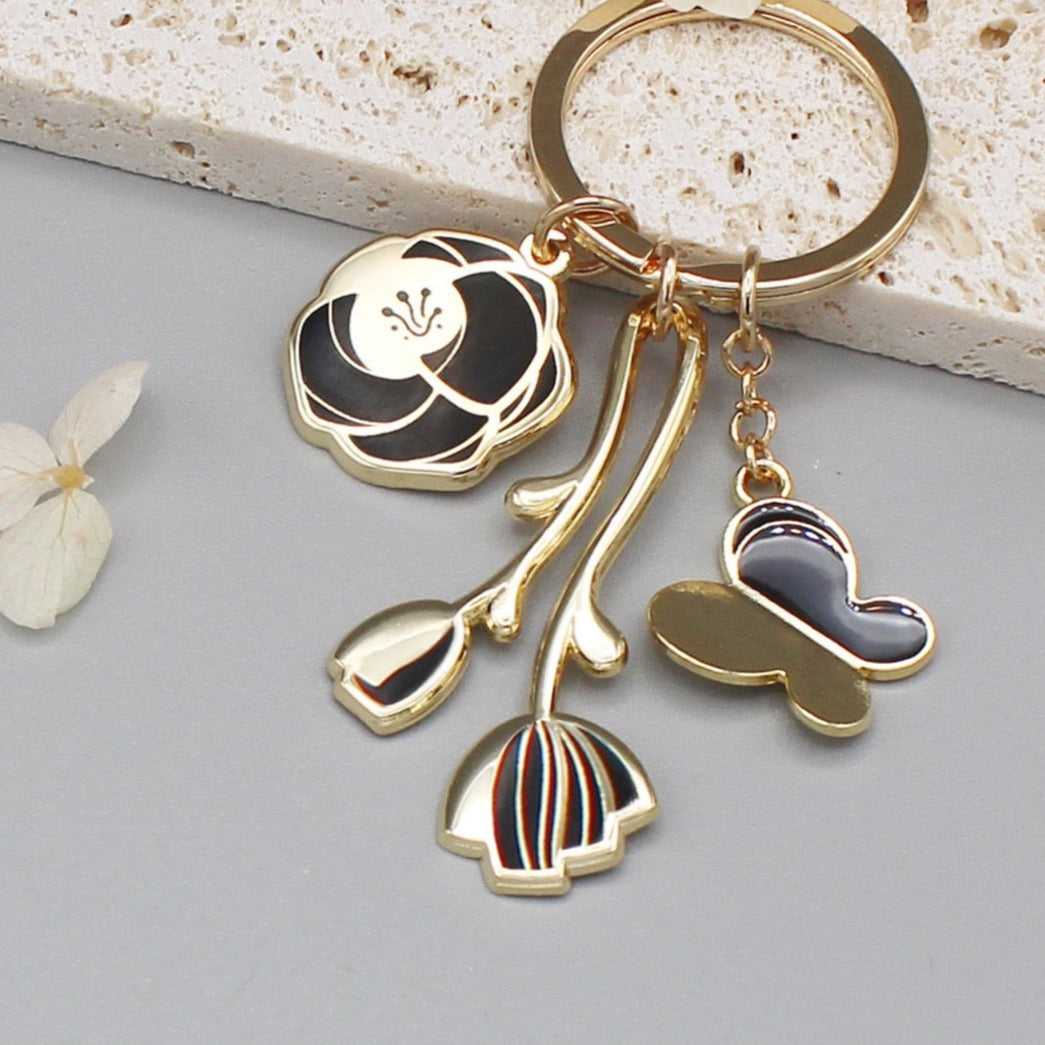 Minimal garden keychain with gold-plated rose, tulip, and butterfly charms in black design.