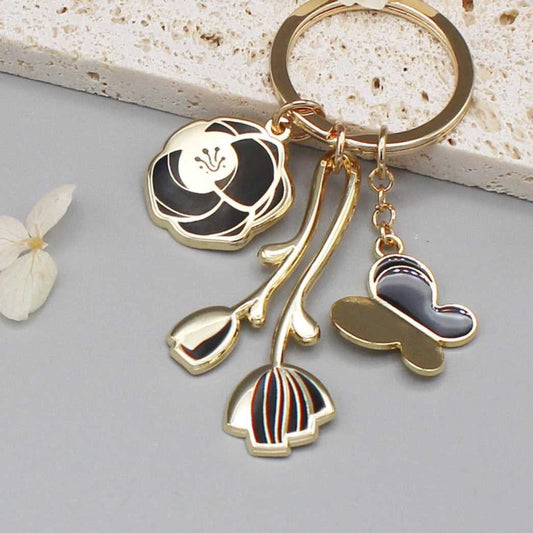 Minimal garden keychain with gold-plated rose, tulip, and butterfly charms in black design.