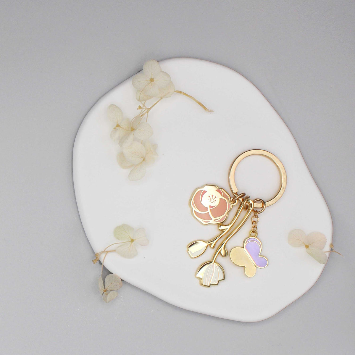 Gold plated minimal garden keychain featuring flower and butterfly charms on a white round display.