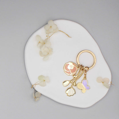 Gold plated minimal garden keychain featuring flower and butterfly charms on a white round display.