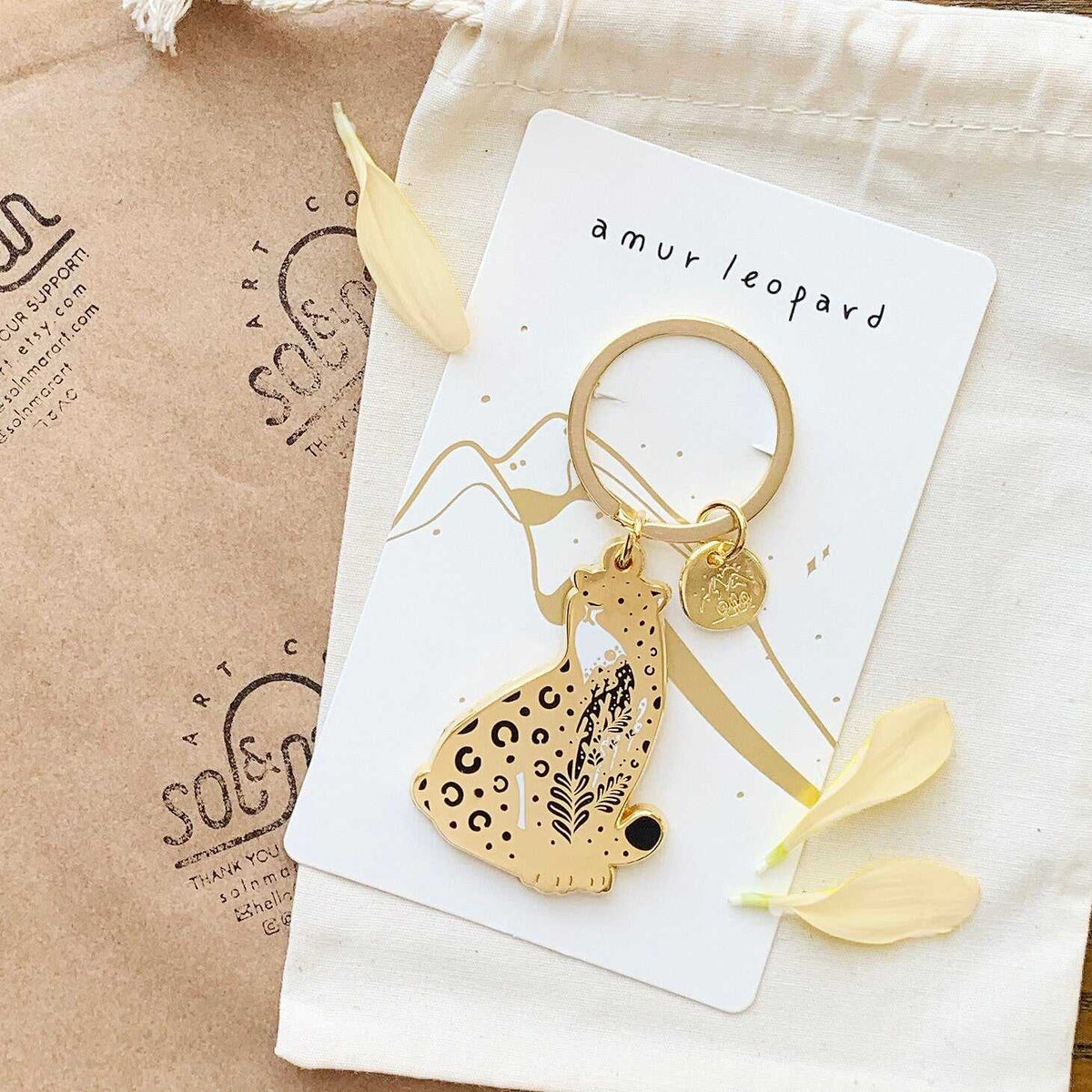 Amur leopard enamel keychain with habitat design on display card for endangered animal awareness.