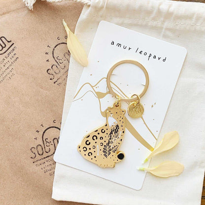 Amur leopard enamel keychain with habitat design on display card for endangered animal awareness.