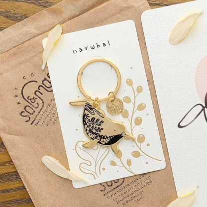 Narwhal enamel keychain on display card showcasing its habitat art, promoting endangered species awareness.