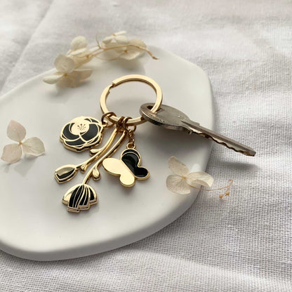 Minimal Garden Keychain with black flower and butterfly charms on a key ring, set on a white dish.